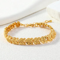 A gold leaf-link bracelet displayed on a textured white surface with a soft white background.