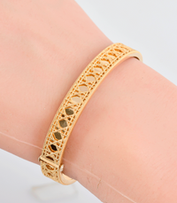 A gold-toned filigree bangle bracelet with openwork cutouts, shown worn on a wrist against a light background.